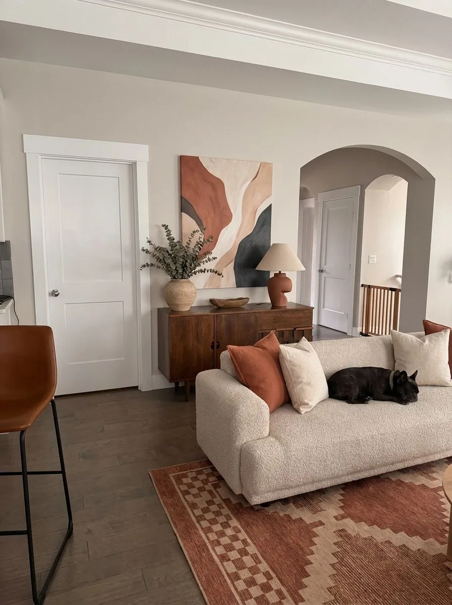 Warm modern living room with cream boucle sofa, rust geometric rug, abstract art, mid-century wood console, terracotta lamp, photorealistic interior design photography, 8k