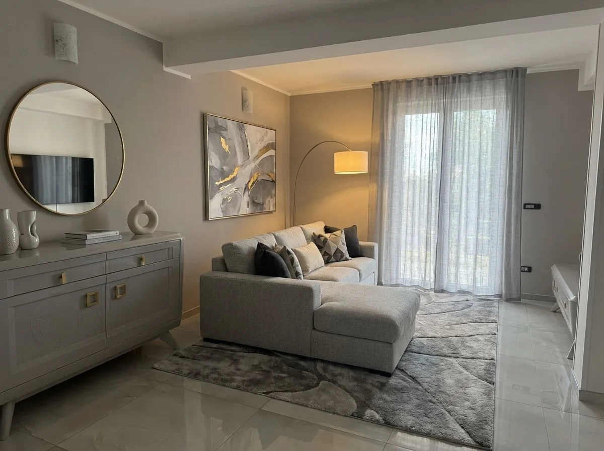 Contemporary living room with light grey walls, sectional sofa, grey patterned rug, gold framed mirror, sheer curtains, photorealistic interior design photography, 8k